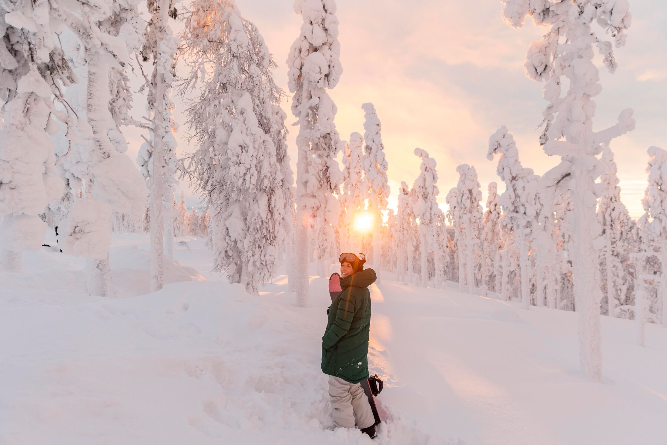 Woman with snowboard standing on snow covered field during sunrise