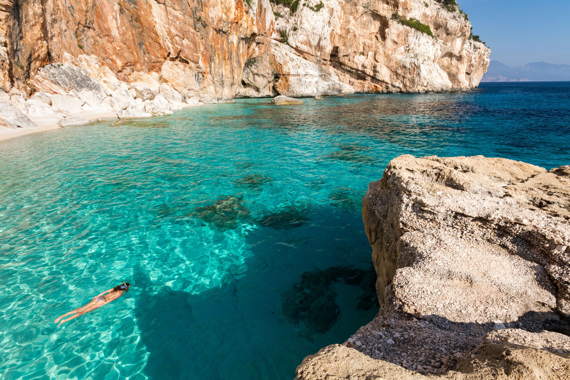 A woman swimming and snorkeling in the clear waters of Cala Mariolu, one of the most beautiful beaches of the east coast of Sardinia.